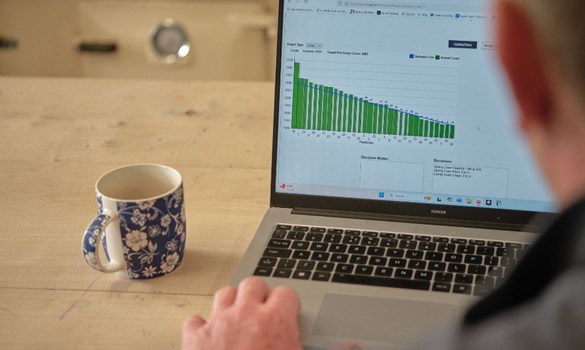 Data on laptop screen and mug of tea on wooden table.